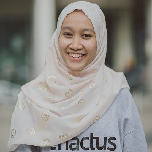 Nur wearing a pale pink and gold hijab, smiling for the camera.