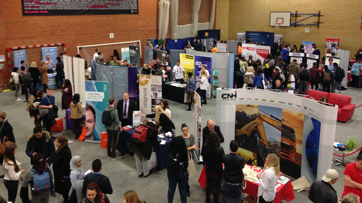 A busy view of the Careers Fair 2016 with lots of students and employers mingling around exhibition stands in the sports centre of the University of Essex 