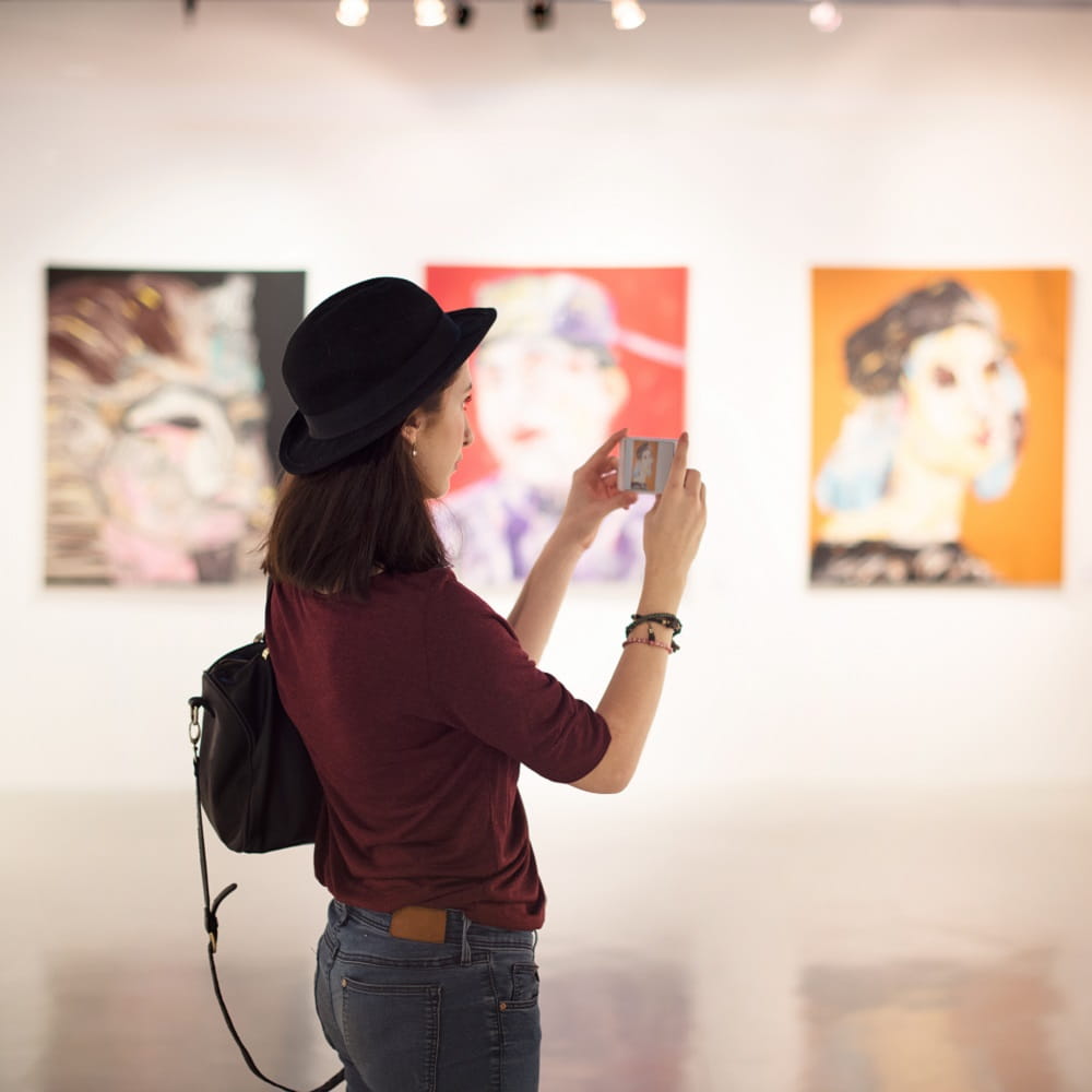 A young woman wearing a hat is taking photographs in an art gallery.