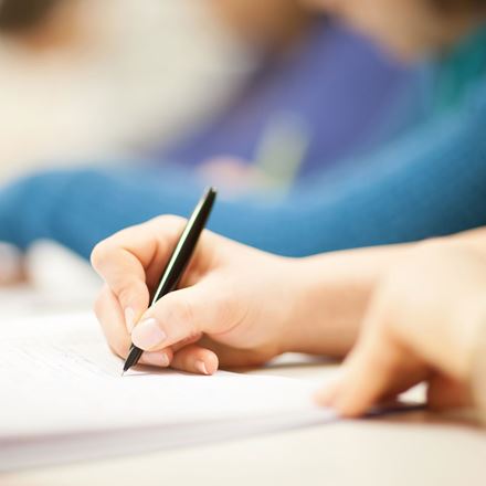 A person holding a pen and writing on a notepad.