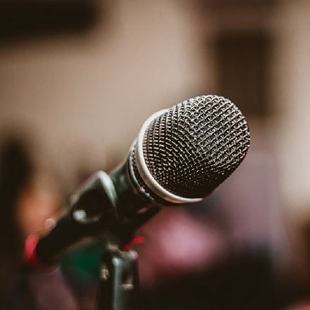 A close up of a microphone with a blurred seminar room in the background.