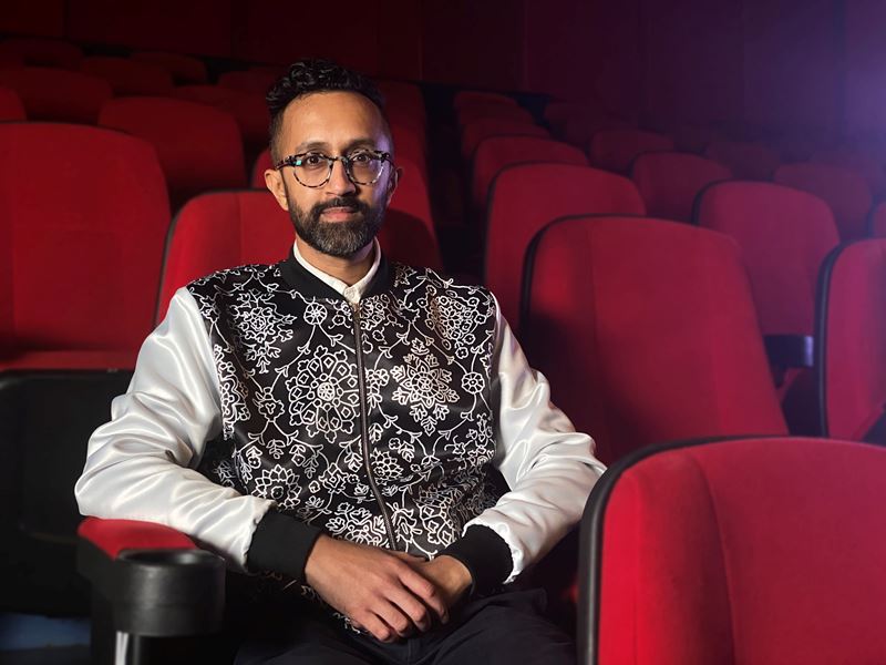 Artist Hetain Patel sits in a cinema theatre of red chairs