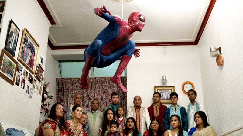 Hetain Patel dressed in a homemade Spiderman outfit leaping off his grandmother’s living room sofa as his extended family look on.