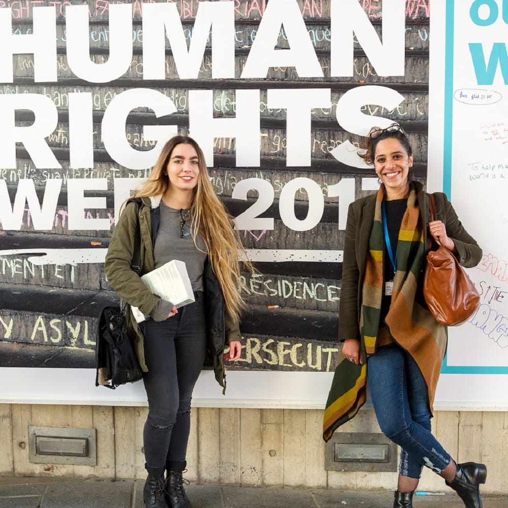Two students standing against Human Rights week poster