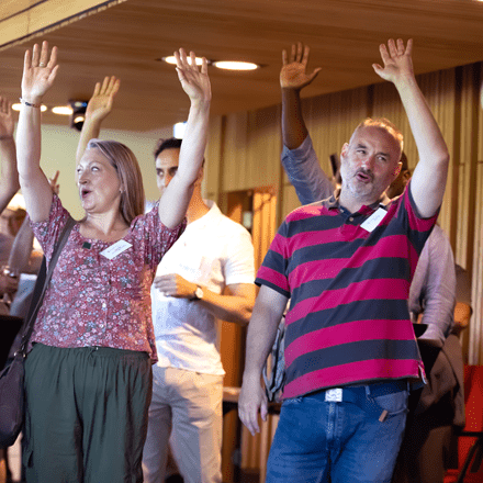 2 people in a group of people all with their hands in the air cheering and smiling