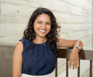Afsheen is stood on a bridge, with her arm resting on it, a brick wall in the background
