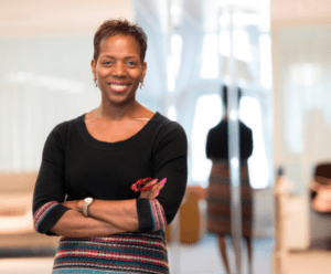 Althea is stood in front of a mirror, her arms are crossed and she's smiling.