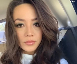 Christina is wearing a white top and is looking ahead to the camera