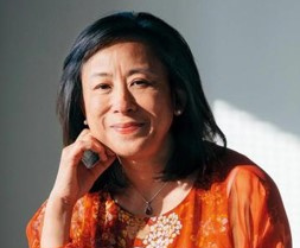 Ellen is sat with her knee up, and her hand resting on the side of her face. She is wearing a bright orange top and the sun is shining over her.