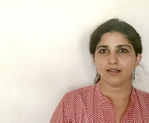 Laya is stood in front of a white wall. She is wearing a red  and white top.