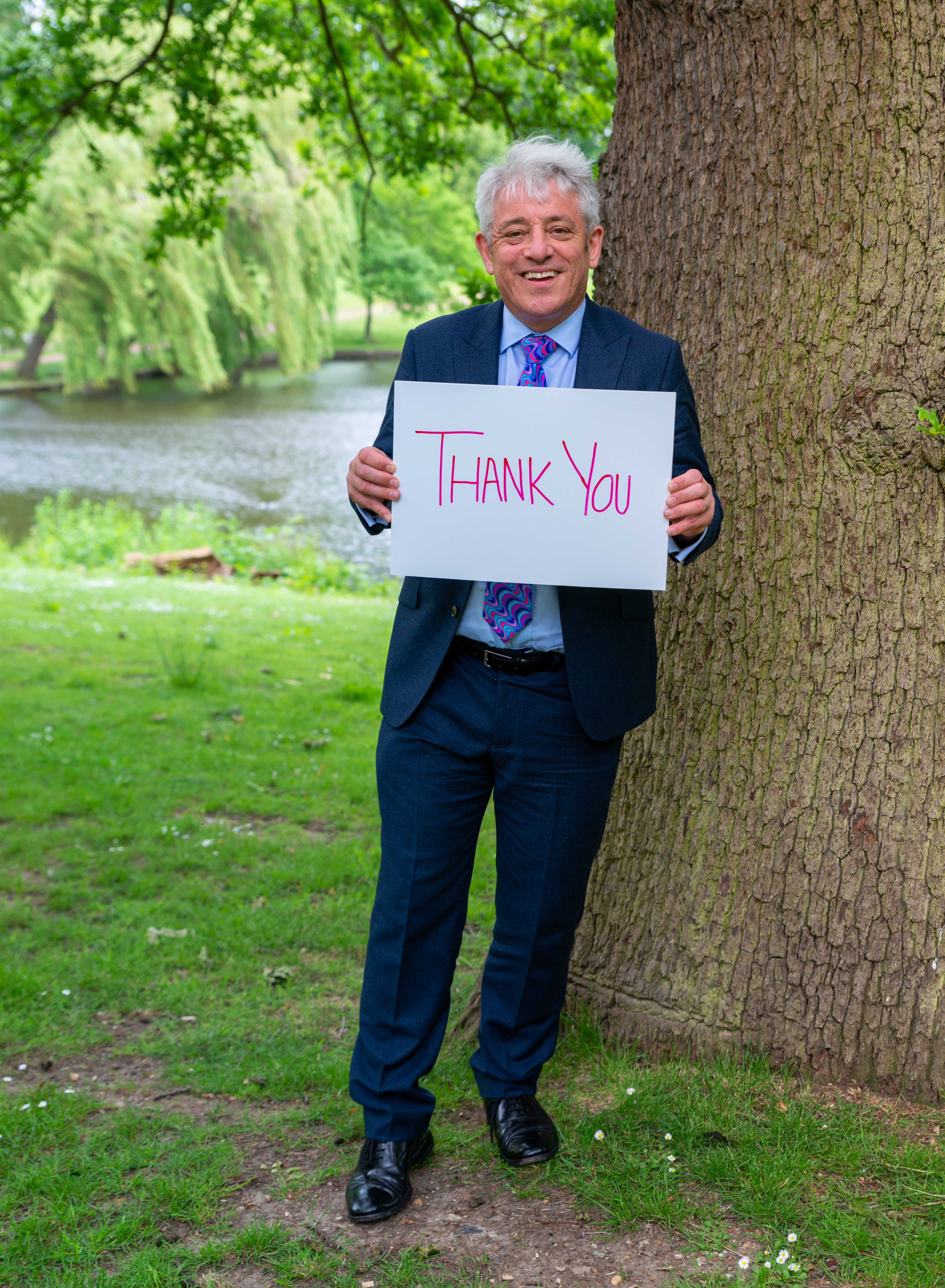 John Bercow on the ground of Wivenhoe Park holding a 'thank you' sign