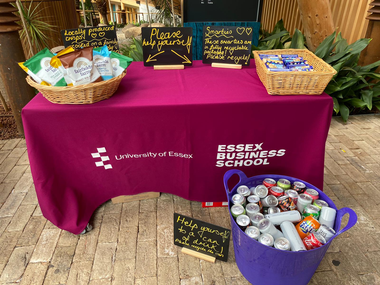 Table with chocolates and crisps on top and a basket of canned drinks in front with signs reminding guests to recycle