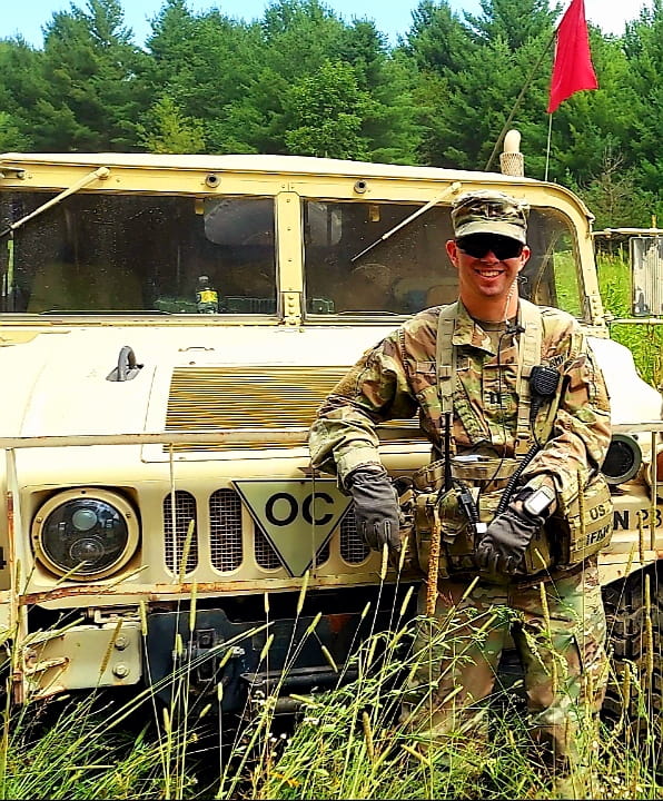MBA candidate Jimmy wearing U.S. army uniform and posing in front of a vehicle 