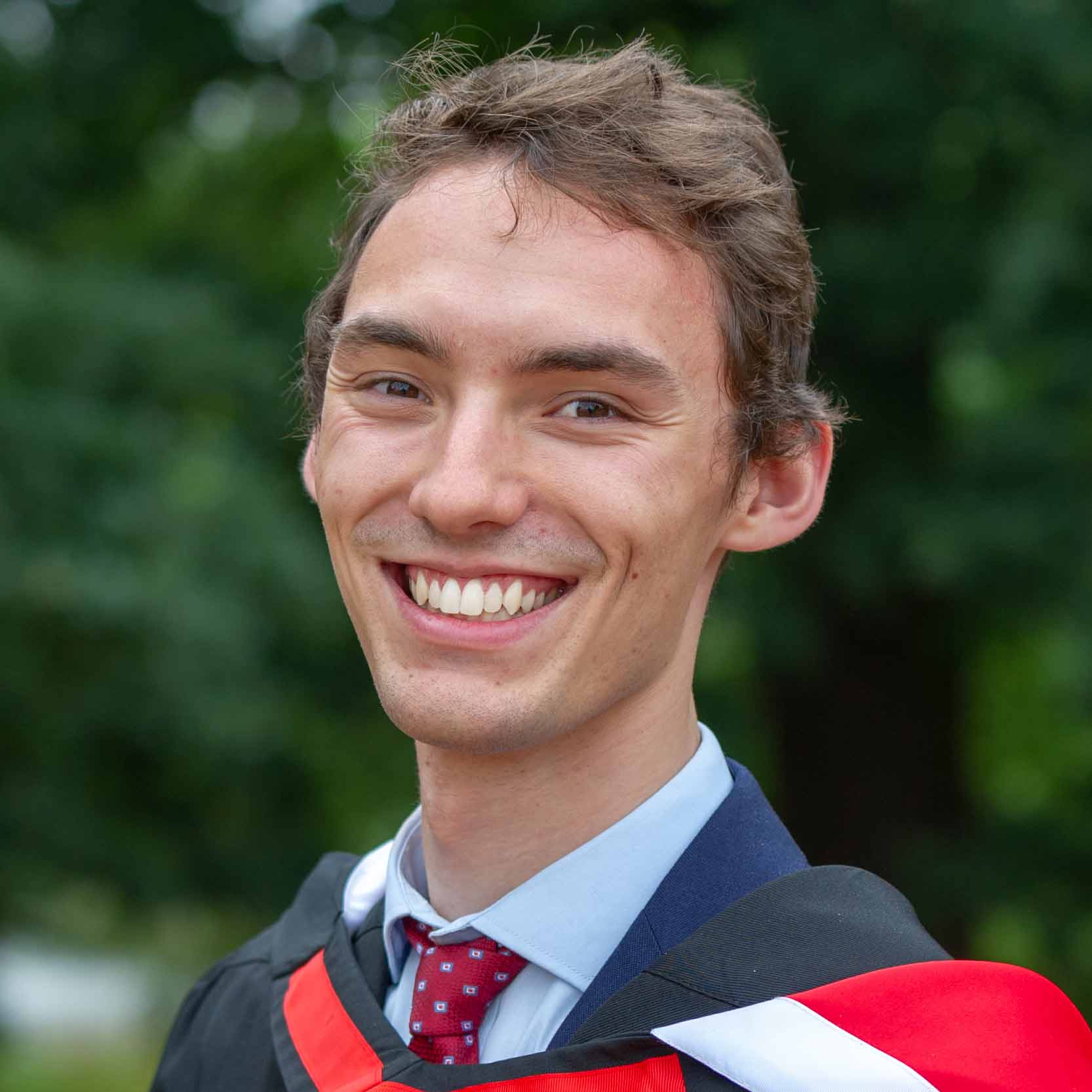 Lewis Smith, smiling, in front of an outdoor, leafy backdrop 