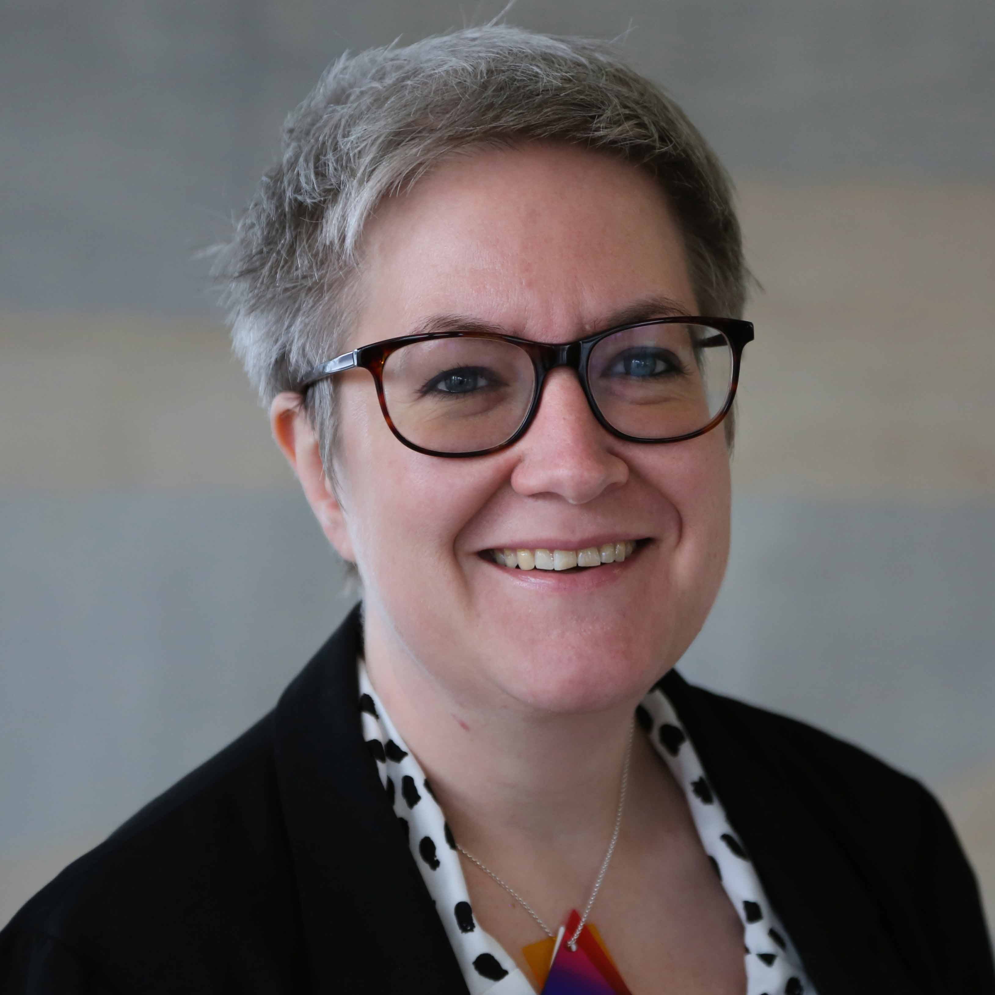 Portrait of Professor Tracey Loughran, smiling and wearing dark rimmed glasses