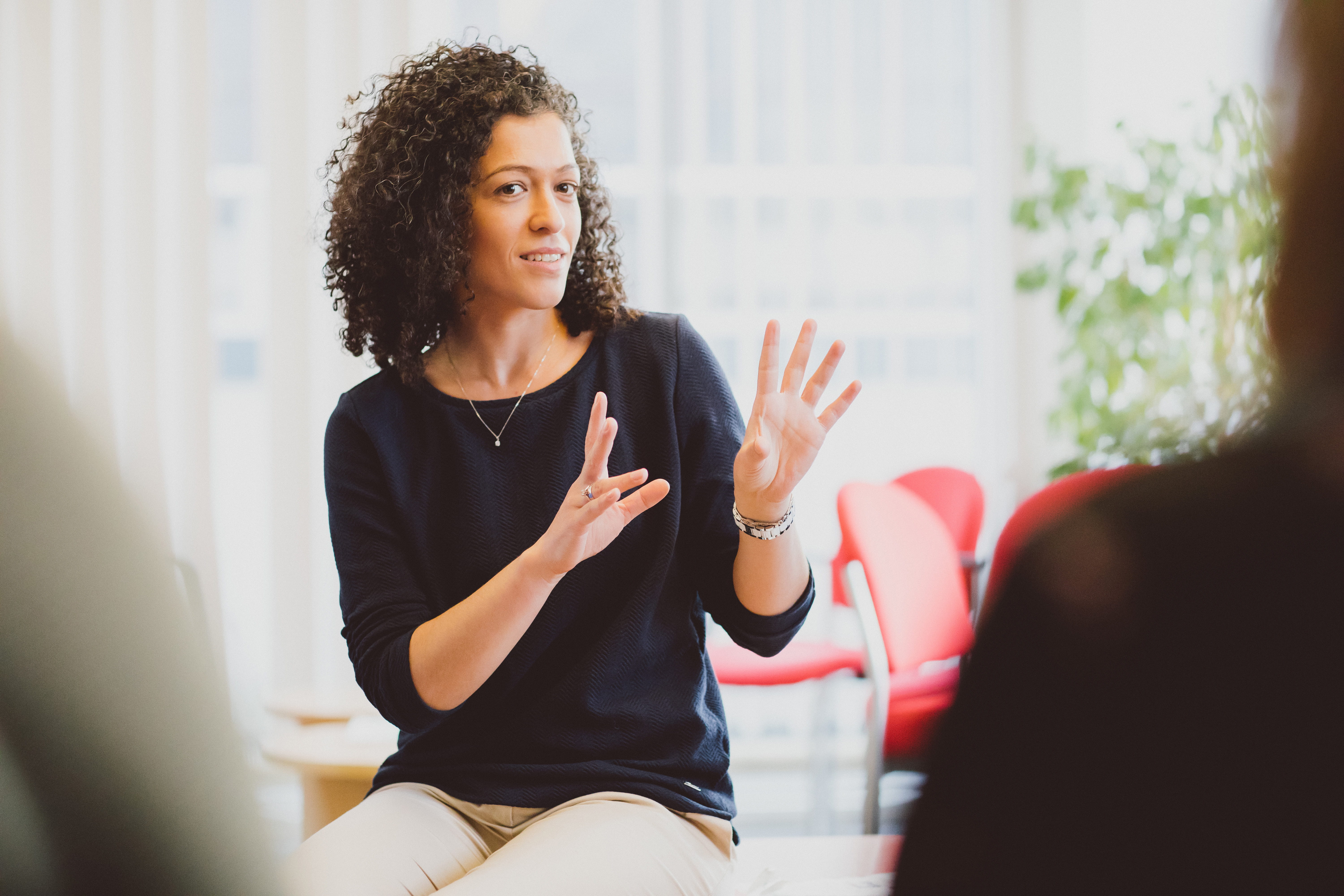 A female lecturer sitting on a table addressing students who are blurred out in the foreground