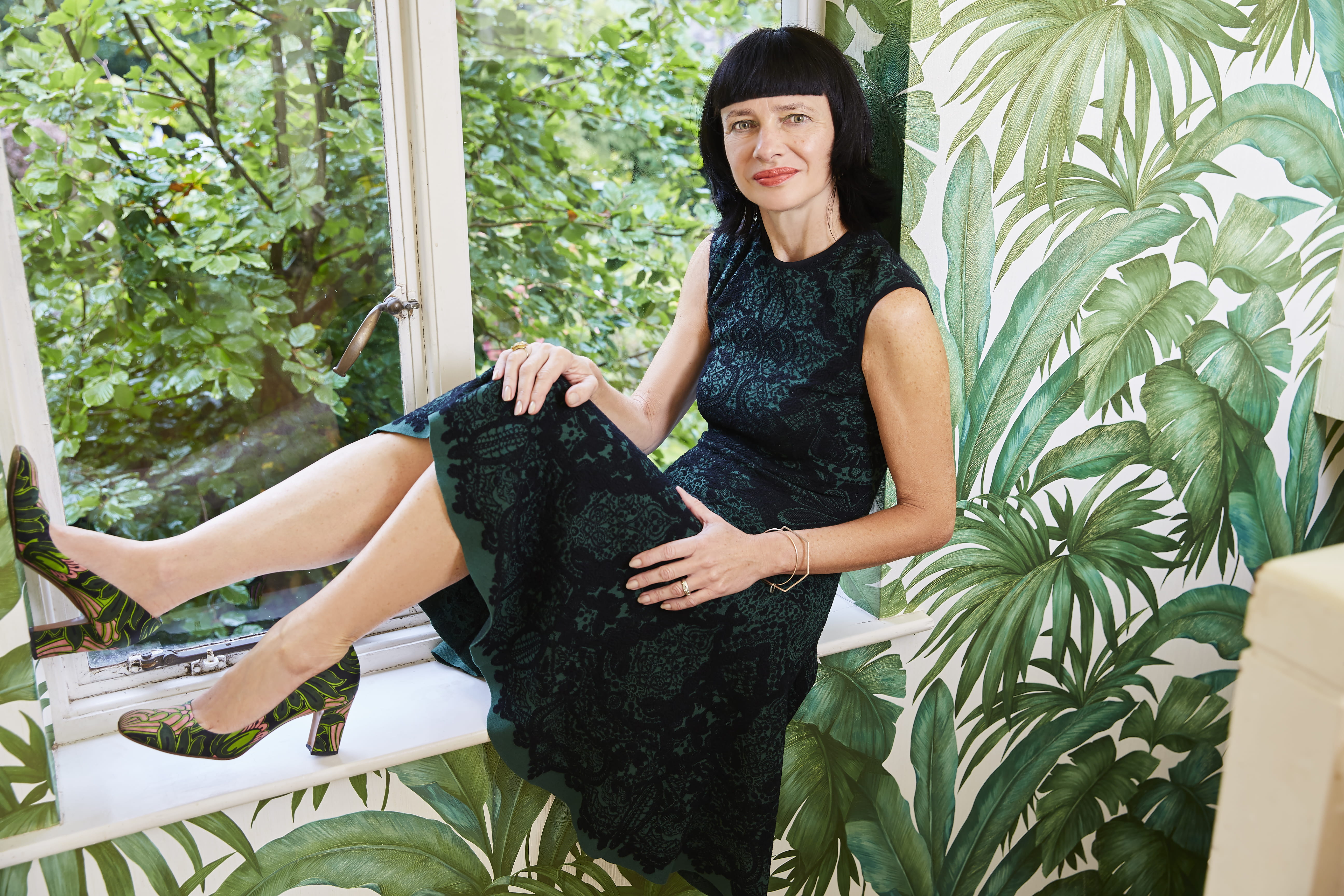 Carry Somers, a woman with dark hair, is sat on a window ledge with a garden visible behind.