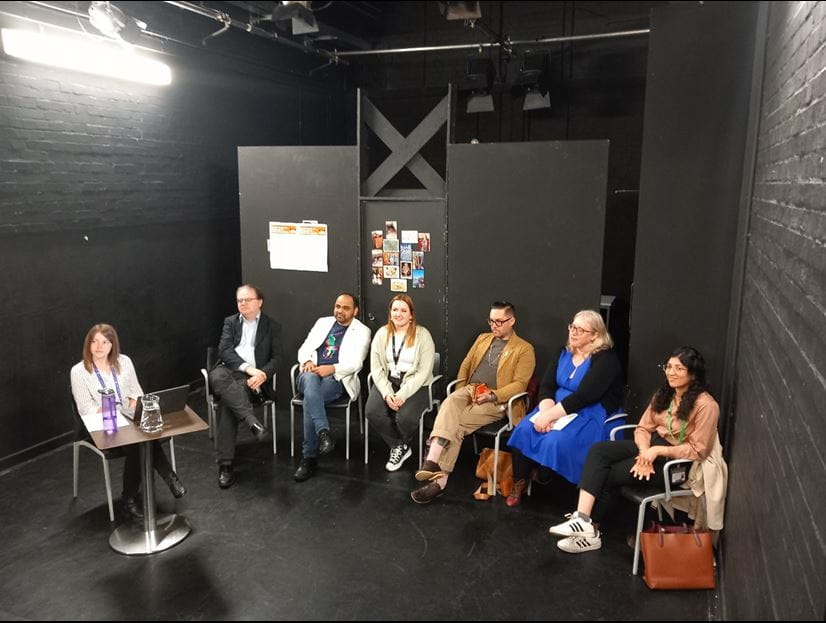 The six panellists, and the host , all seated and looking up to the audience. 