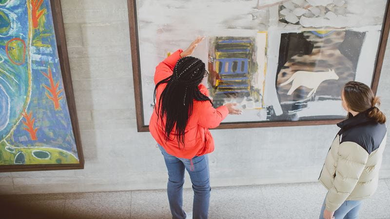 ESCALA Art on display in the Silberrad student centre with two female students viewing.