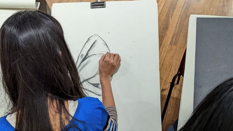 A young woman with dark hair attends a life drawing class