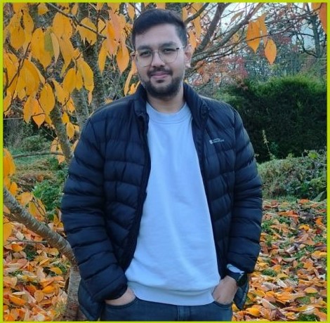 Nikil Patel standing outside with his hands in his pockets, a tree with yellow leaves is behind him.