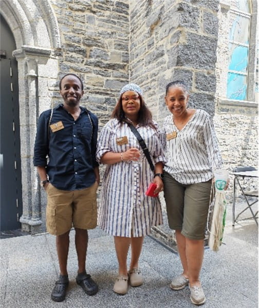 Dr Crispus Mbaluto, Dr Charlene Dambire, and Professor Yoselin Benitez-Alfonso, standing outside with a large stone building in the background.
