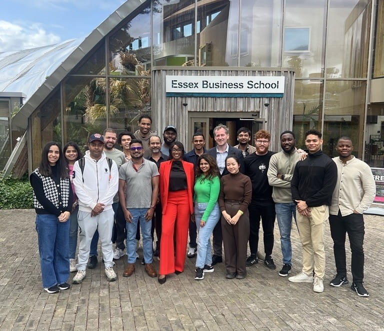A group photos of Chisola Chitambala with MBA students, standing outside the Essex Business School building.