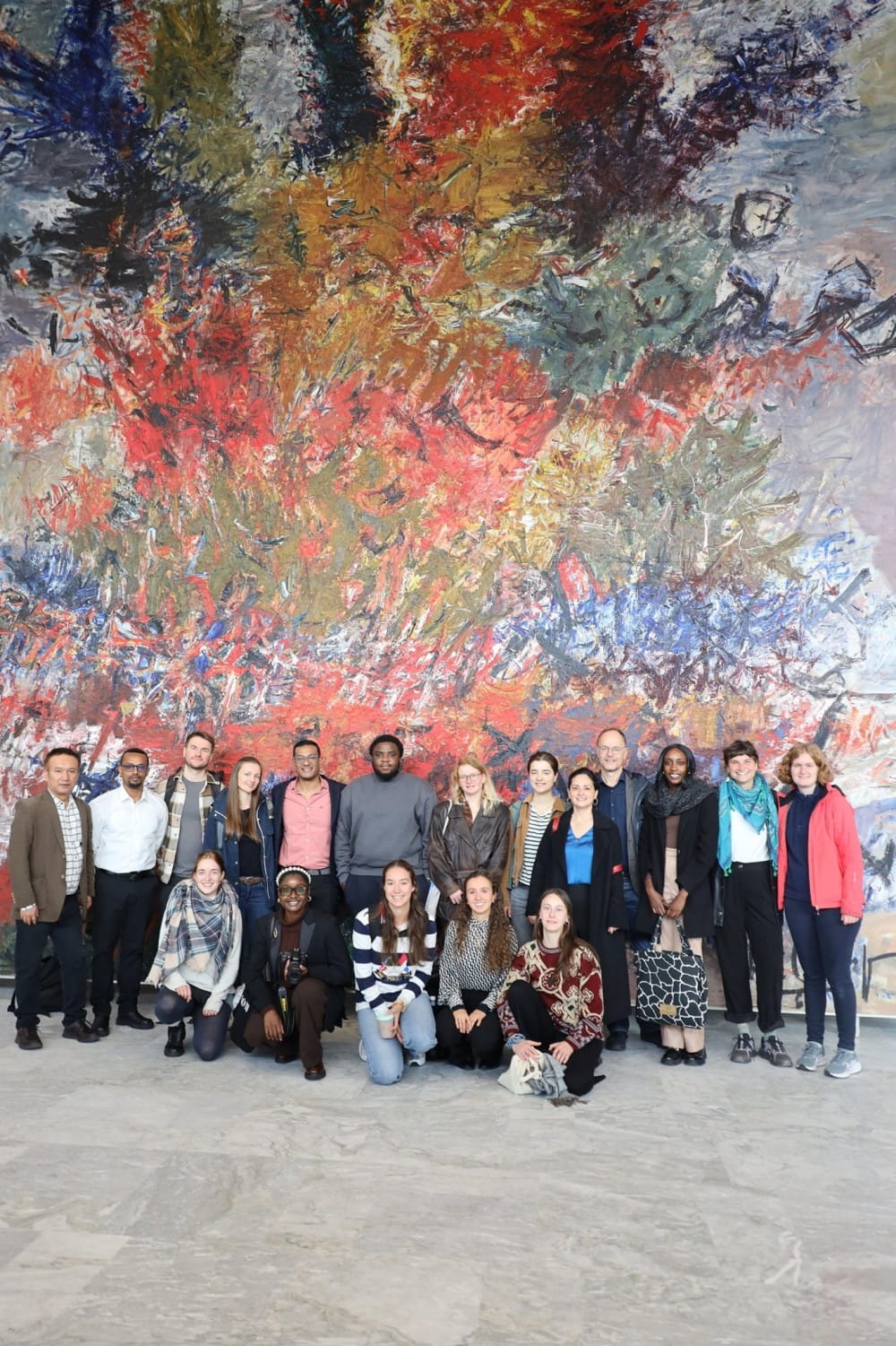 A group of staff and students standing in front of a large abstract artwork, which covers the whole wall behind them.
