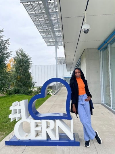 Rebecca Adut Dau standing next to a sign that says "#I heart CERN".