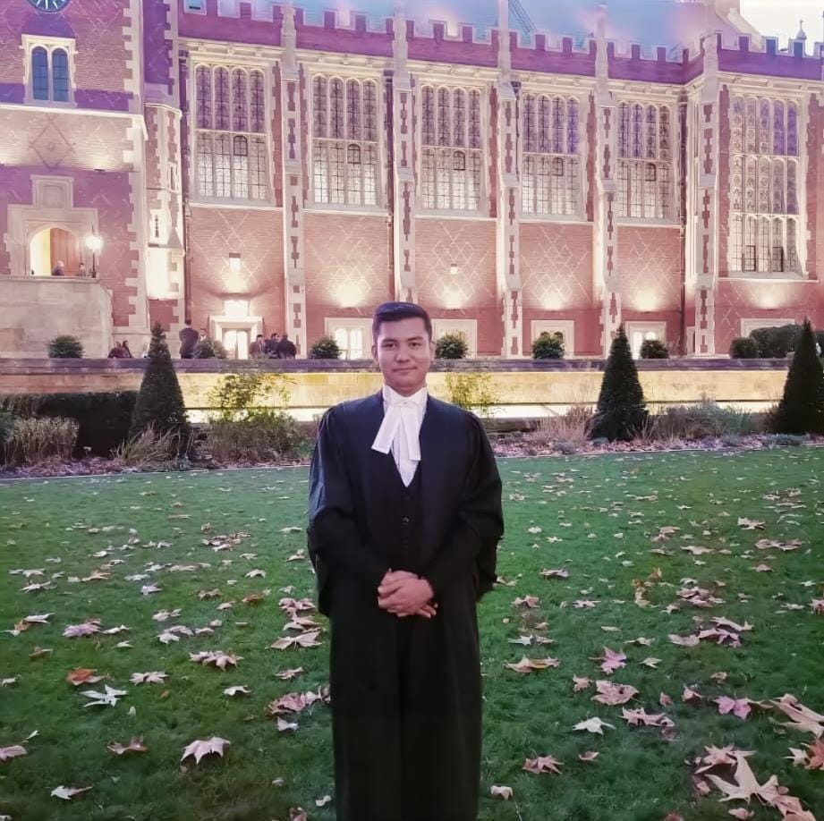 Eayan passing the Bar stood outside an old building lit up. Leaves scatter the floor behind him