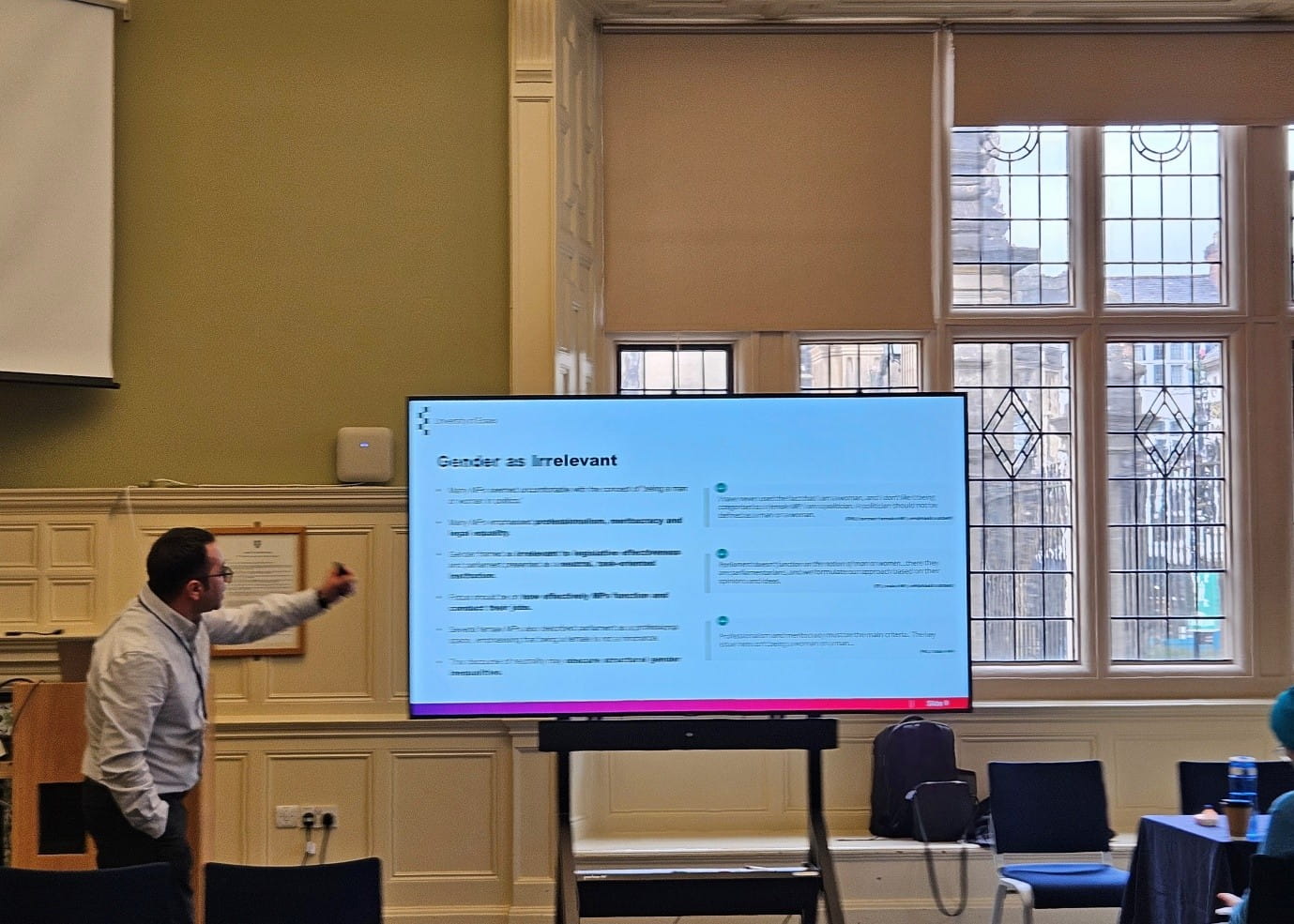 Farid Adilov standing at the front of a room pointing at a screen showing a slide from his presentation.