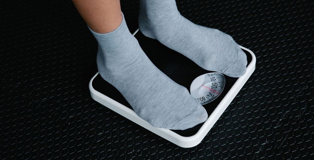 A pair of feet in light grey socks standing on black scales to find out the persons weight.