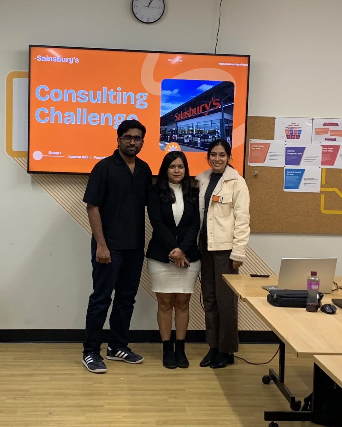 three people in front of a tv screen that reads 'consulting challenge'