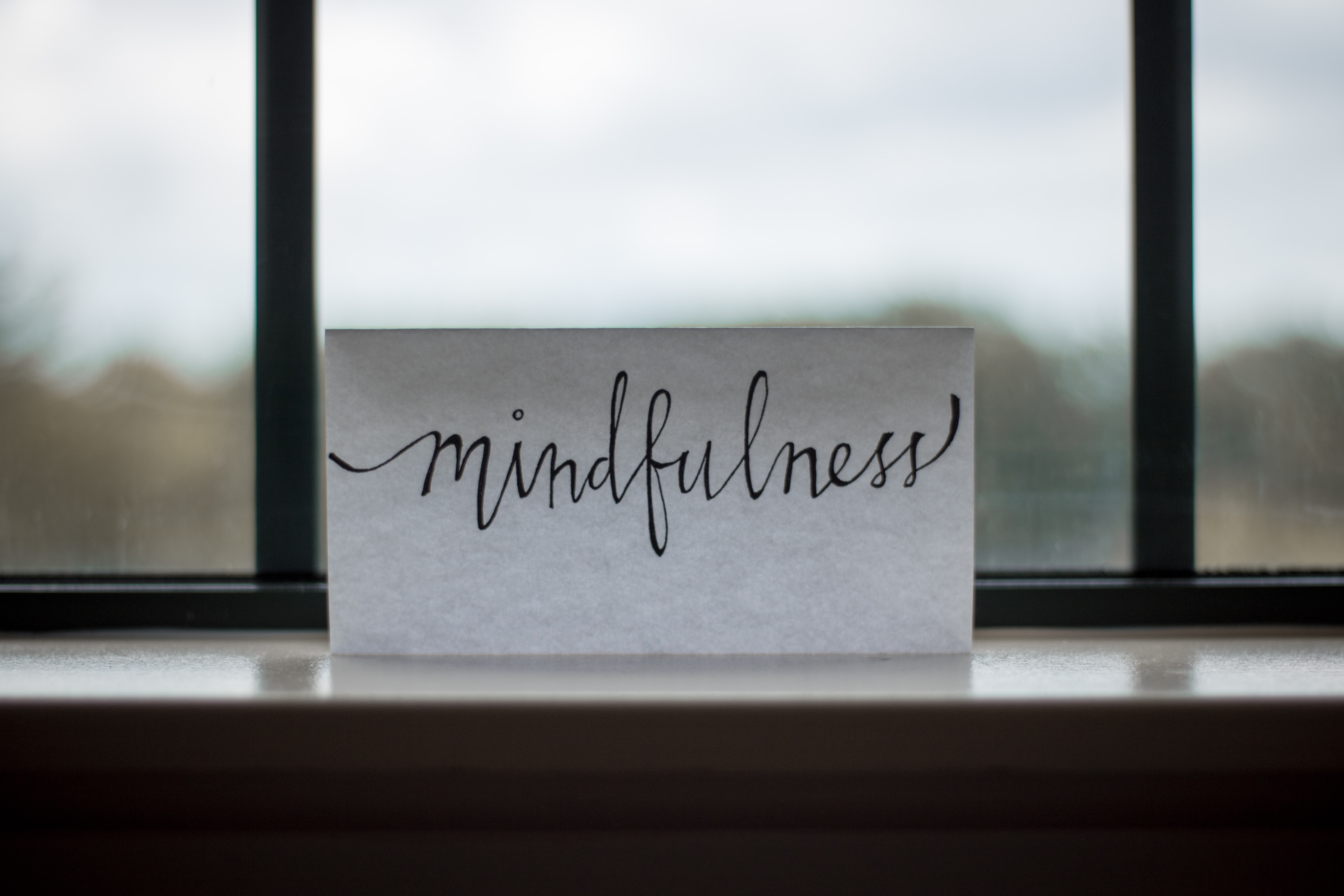 A sign with 'Mindfulness' handwritten on it in cursive script against a window