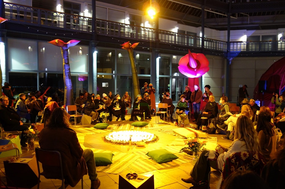 photo of circle of delegates from across the world in a circle with candles in the middle surrounded by large inflatable flowers