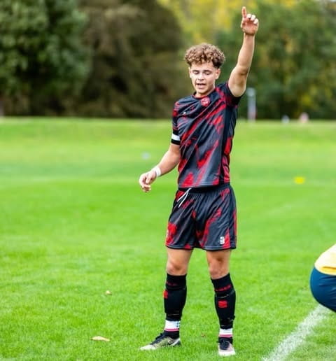 University of Essex football scholar Cameron Button representing Essex Blades men's football team on a grass pitch by the white sideline with arm raised in the air