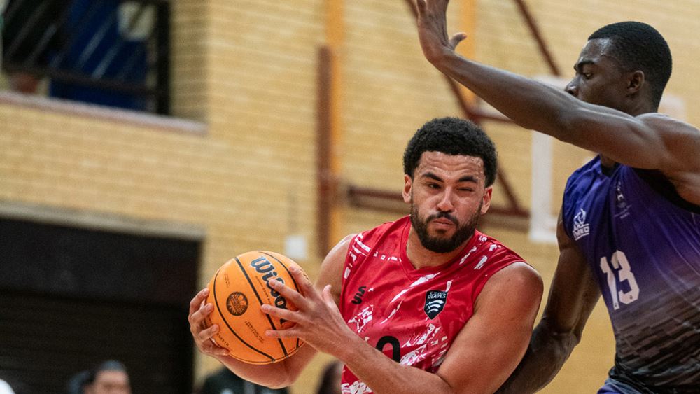 Luke Busumbru running with basketball in hands dodging opposing player