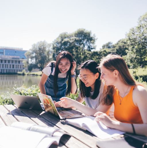 Students sit and smile as they work next to the lake at our Colchester Campus.