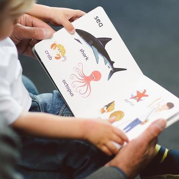 A young child is learning to read from a book with a parent