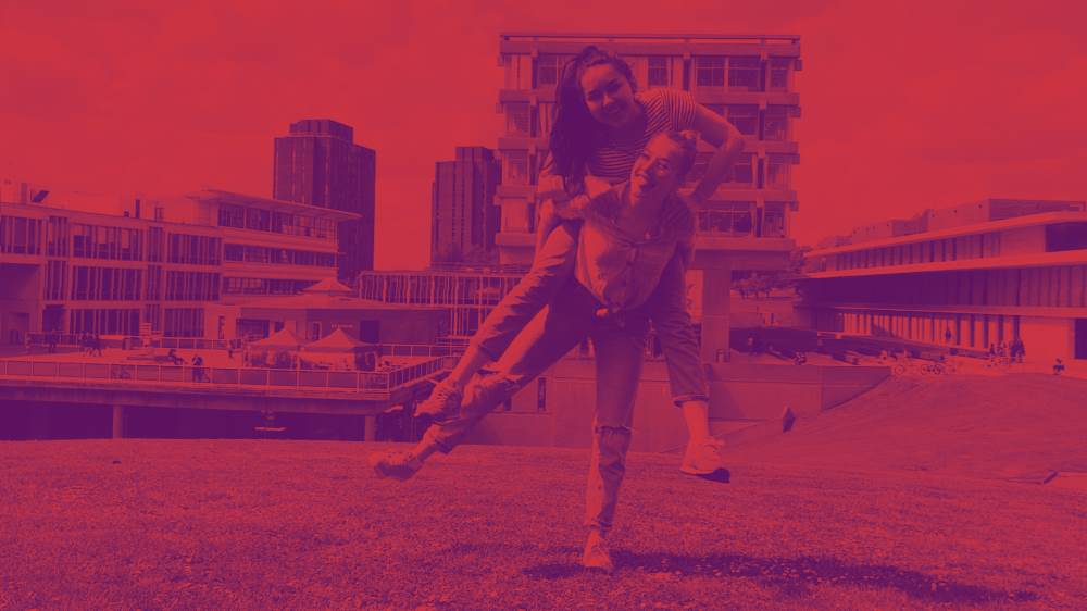 A student giving another student a piggy back on campus. Picture edited with a red and purple gradient colour tone.