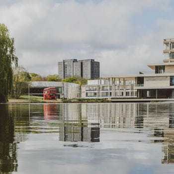 A photo across a lake, with buildings in the background and their reflection in the water of the lake.