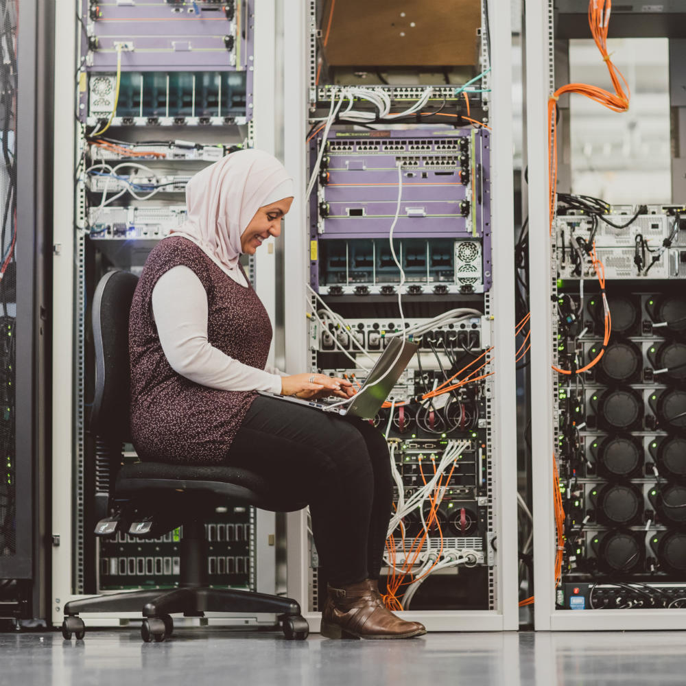 Image of a female computer science and engineering researcher on a laptop in a networks lab.