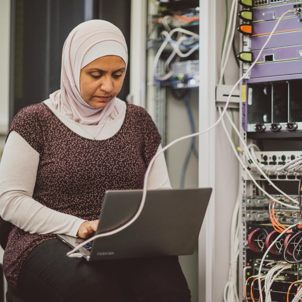 Dr Mays Al-Naday working on a laptop that is connected to some servers on her right.