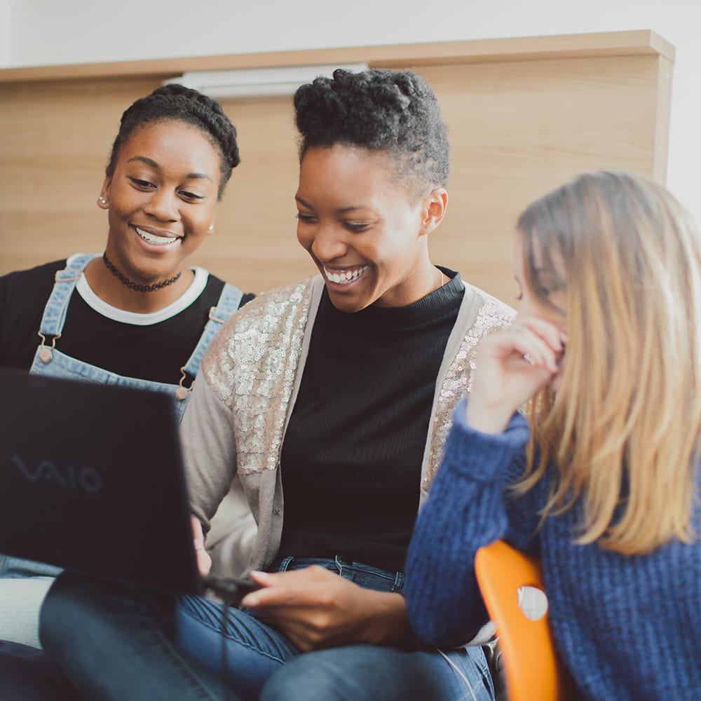 Three female students looking at a laptop together smiling