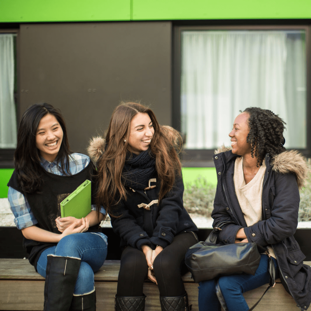 Photo of three students chatting on a bench