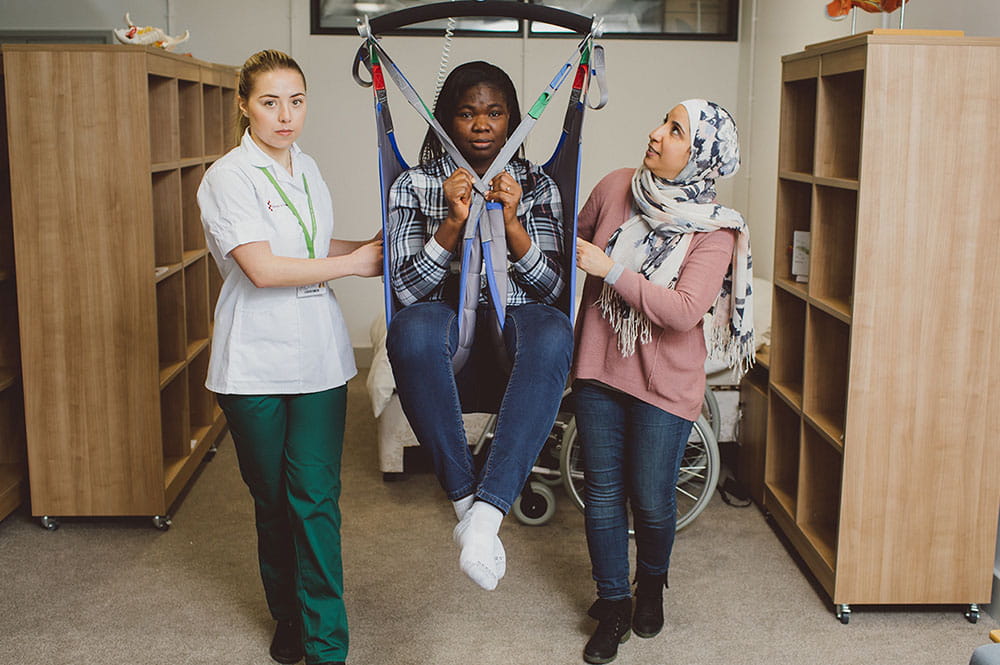 OT students using a ceiling hoist to move a patient from the bedroom to the bathroom