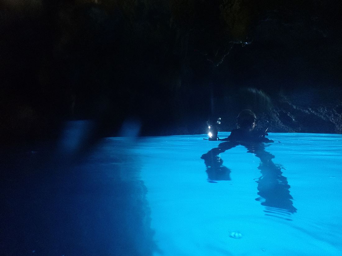 scuba diver floating in an illuminated cave pool