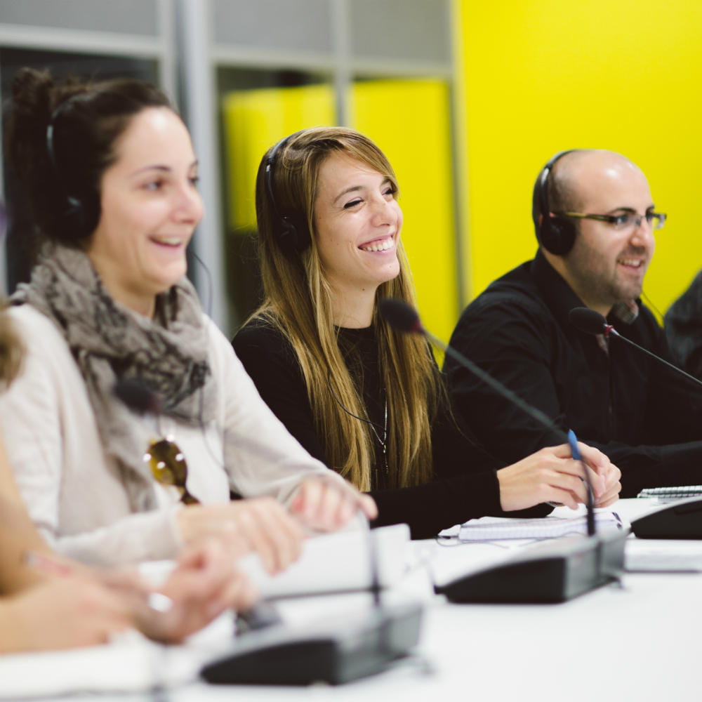 Three people sitting in a row at desks with microphones and wearing headphones.