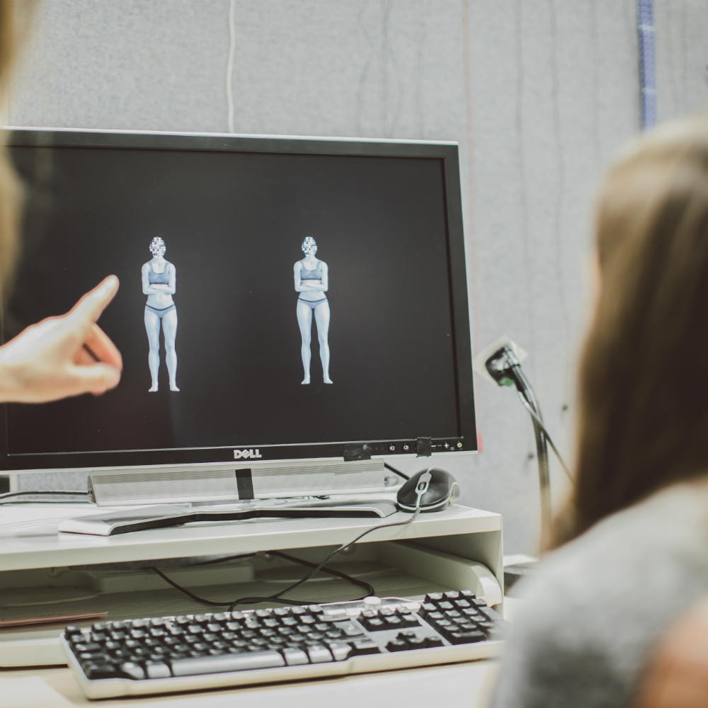 An over-the-shoulder shot of a computer screen showing two figures, with someone to the left reaching across to point at one of the figures.