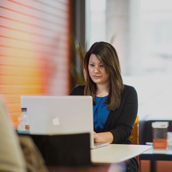 This is an image of a female student sitting at a laptop in a cafe.
